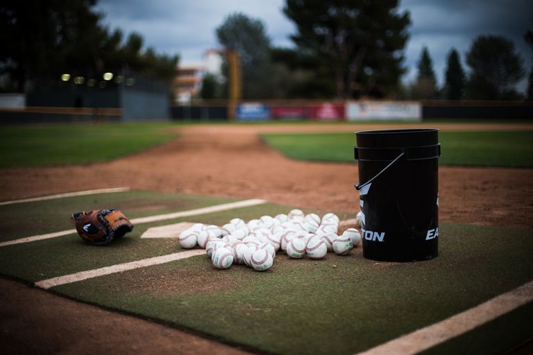 Baseballs sitting on the pitchers mound next to a baseball glove and a bucket
