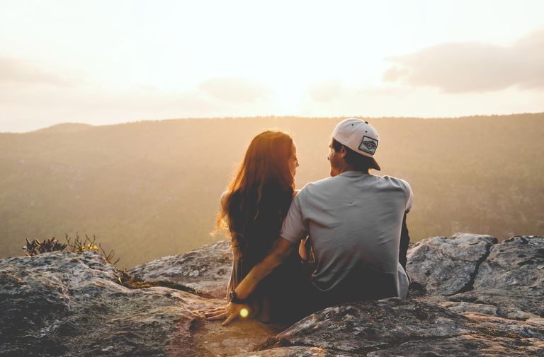 A couple sitting on a rock in front of a hill during sunset