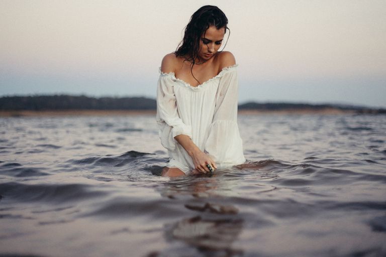 a confident woman standing in water wearing a white shirt