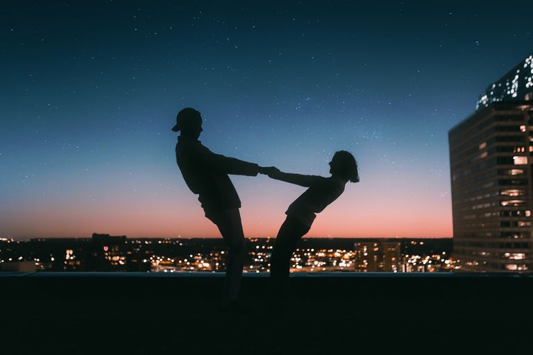 Silhouette of couple holding hands at night in front of a city