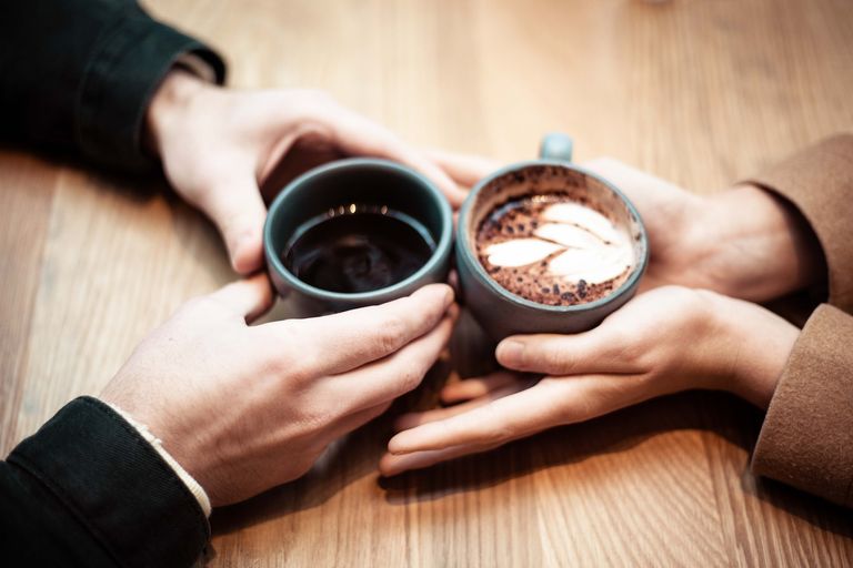 2 people holding cups of coffee with their hands touching