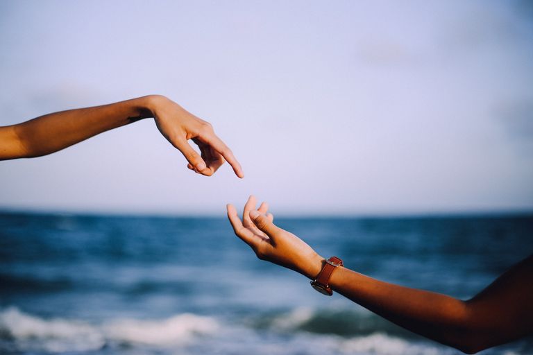 Two hands about to touch in front of the ocean