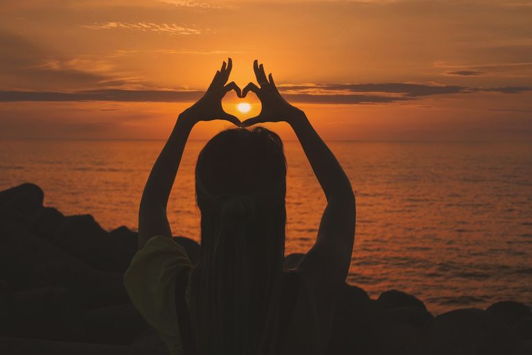 a woman making a heart with her fingers with the sun in the middle of the heart