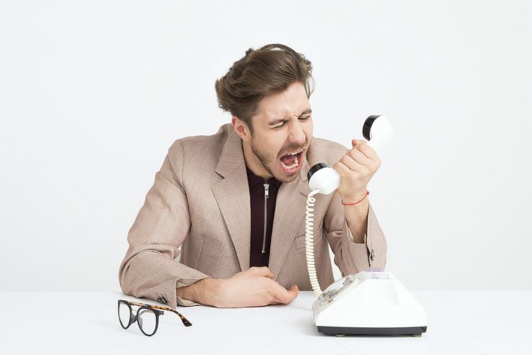 A man in a suite yelling into a white rotary phone