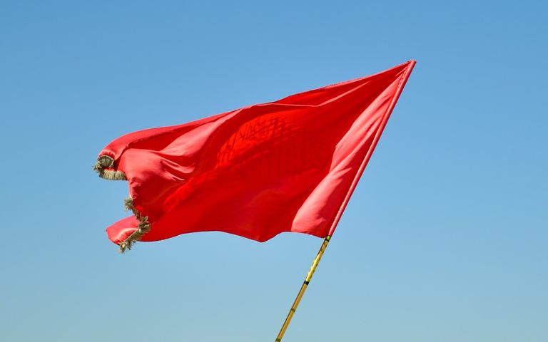 A red flag flapping in the wind with the sky as a background